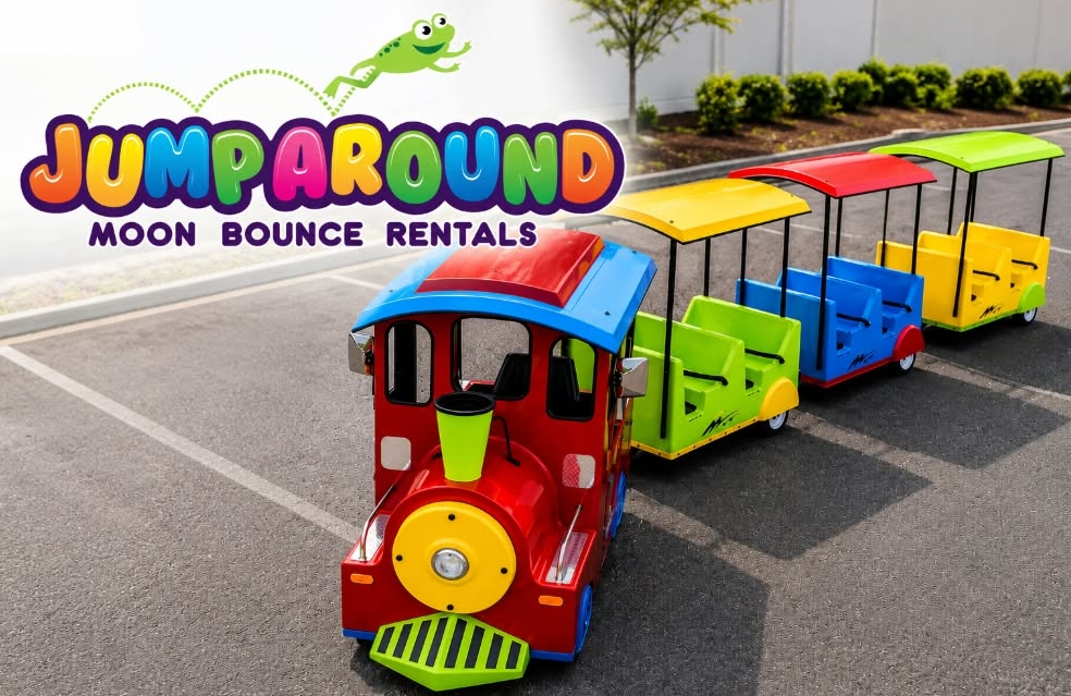 Trackless train ride rental with three colorful passenger cars, an inflatable archway, and a train conductor operating outdoors on asphalt.
